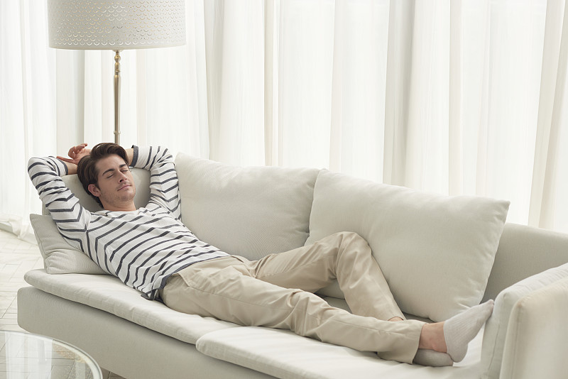 一个男人躺在客厅的沙发上睡觉图片素材