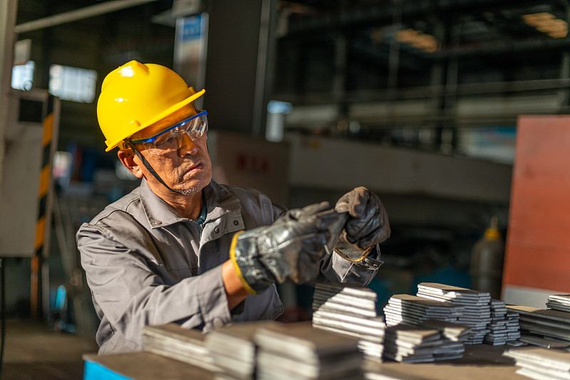 阳光下厂房里带安全帽检查零件的技术工人图片下载