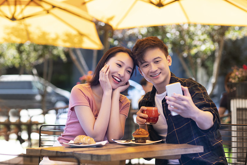 年轻情侣在户外咖啡厅用手机自拍图片下载