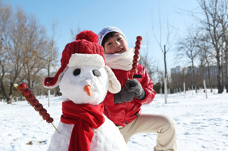 男孩拿着糖葫芦和雪人在雪地上图片素材