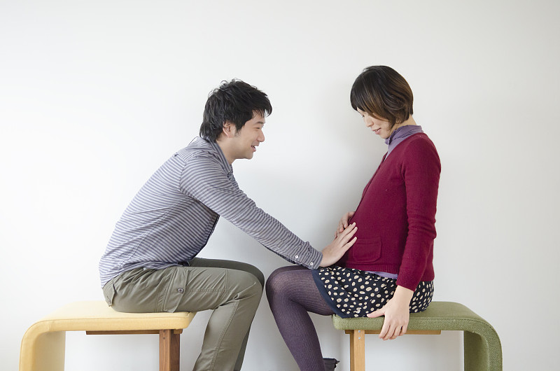 夫妻面对面坐着，丈夫抚摸怀孕妻子的腹部图片下载