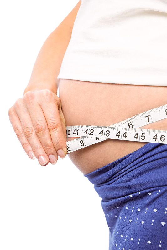 一名孕妇在白色背景下测量自己的肚子图片下载