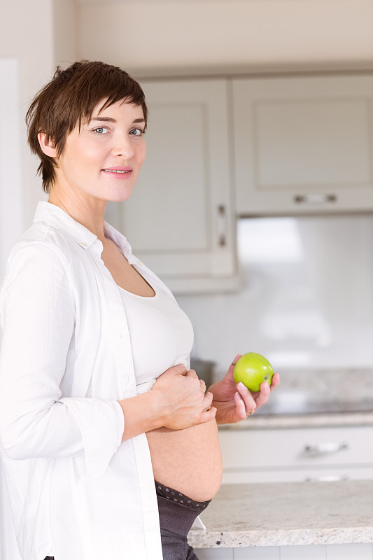 一个孕妇在厨房里拿着苹果图片素材