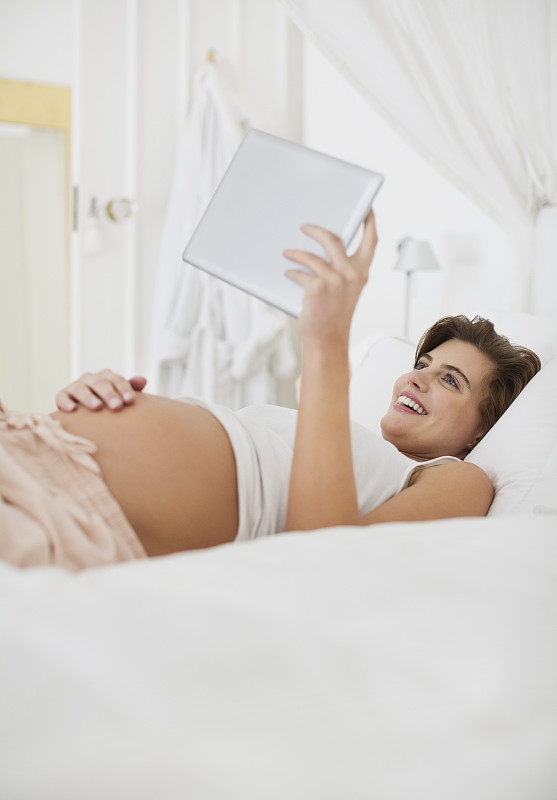 孕妇在床上使用平板电脑图片素材