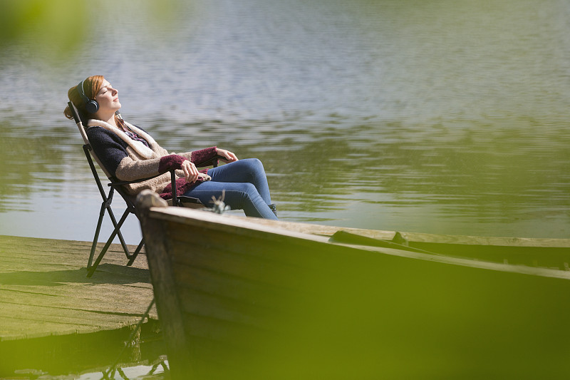 宁静的女人放松听音乐耳机在阳光明媚的湖边码头图片素材