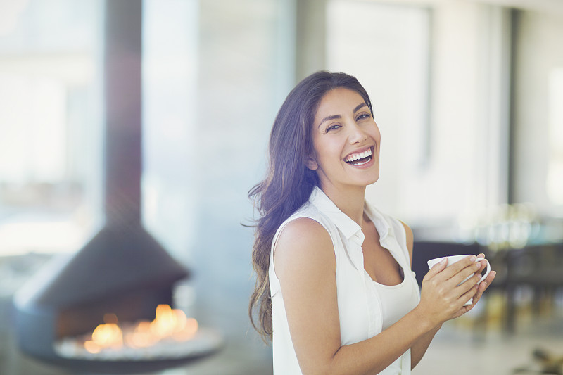 肖像微笑的女人在壁炉旁喝咖啡图片素材
