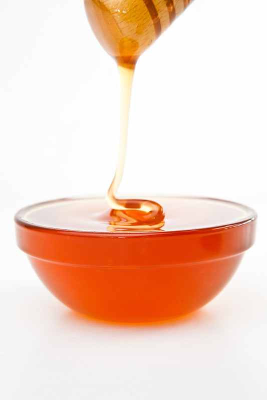 蜂蜜在白色的背景下滴落在装满蜂蜜的碗里图片素材