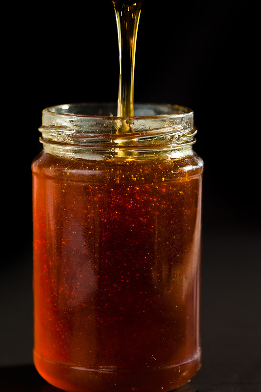 蜂蜜在黑色的背景下滴落在蜂蜜罐中图片素材