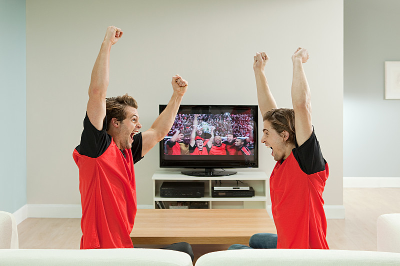 两个年轻人穿着足球衫在电视上看足球比赛图片下载