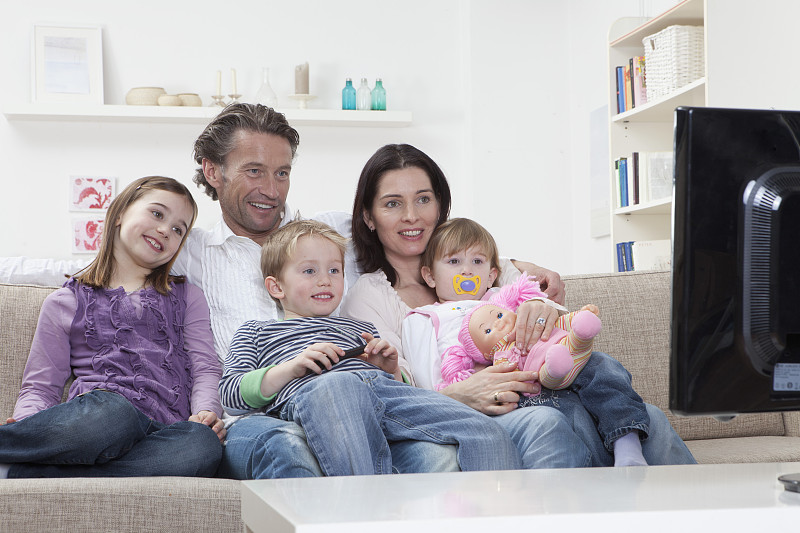 德国，巴伐利亚，慕尼黑，一家人坐在沙发上看电视，面带微笑图片下载