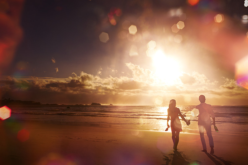 一对情侣沿着海滩散步，夕阳下的剪影图片下载