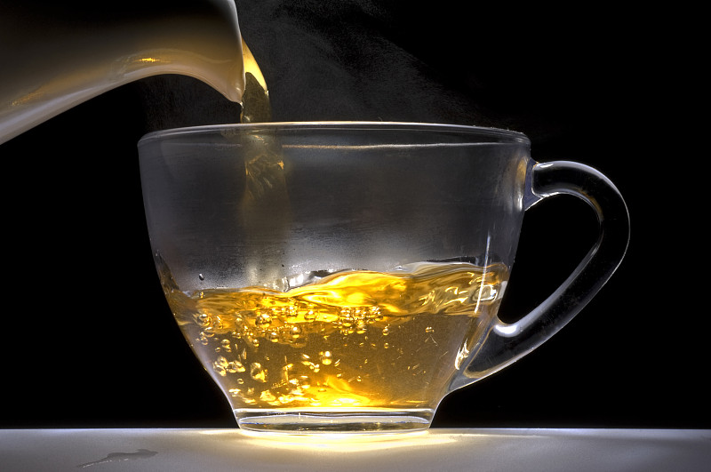 茶水从白色瓷壶倒入玻璃杯中。图片下载