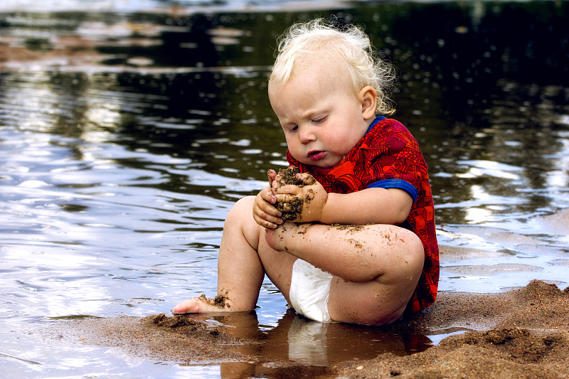 一个小孩坐在海边的水里图片下载