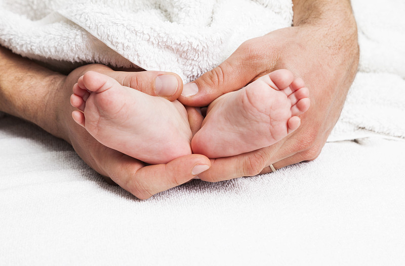 爸爸的手牵着宝宝的脚。美丽,柔软和小。图片下载