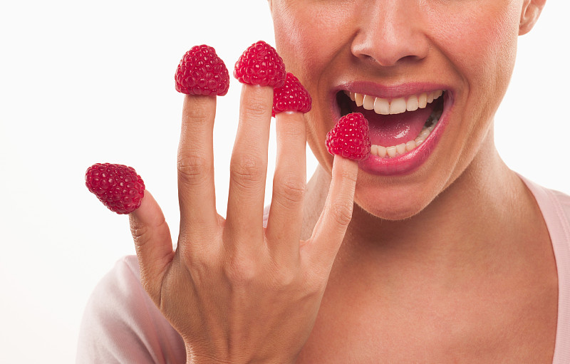 近距离的女人咬树莓的指尖图片下载