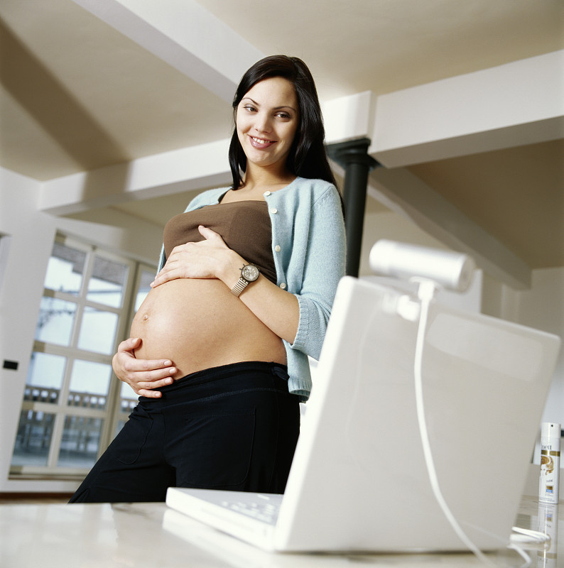 年轻孕妇微笑着向网络摄像头展示自己的肚子图片下载