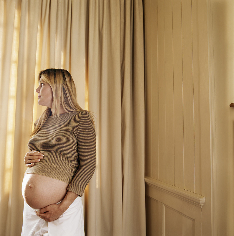 一个孕妇站在帘子旁，看着别处图片下载