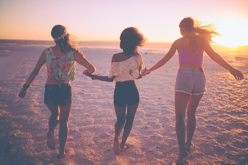 日落时分，在海滩上牵着手跑步的女性朋友们图片下载
