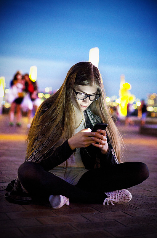 微笑的年轻女子在晚上用智能手机发短信，东京图片下载