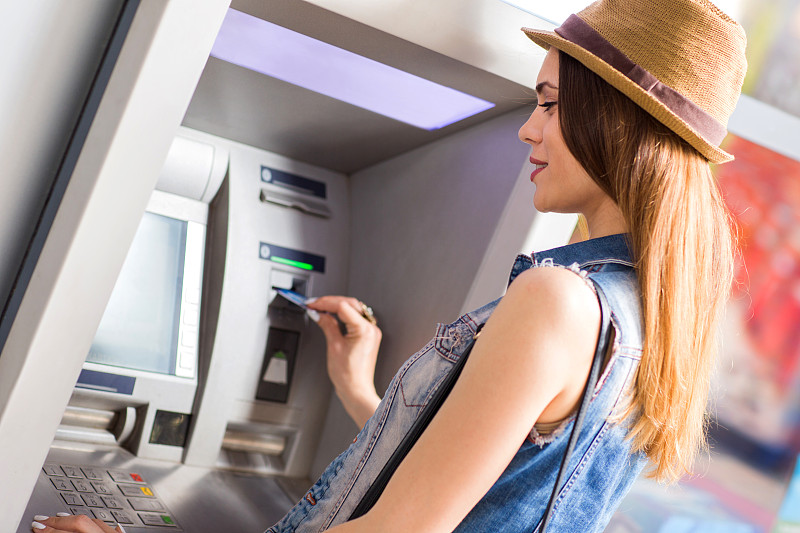 微笑的年轻女子正在自动取款机上取款。图片素材