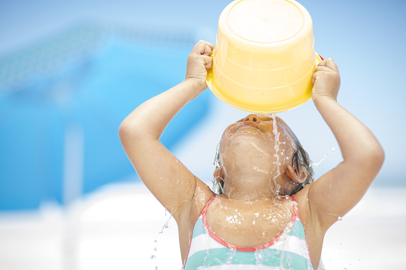 Girl on beach splashing herself with a bucket of water图片素材