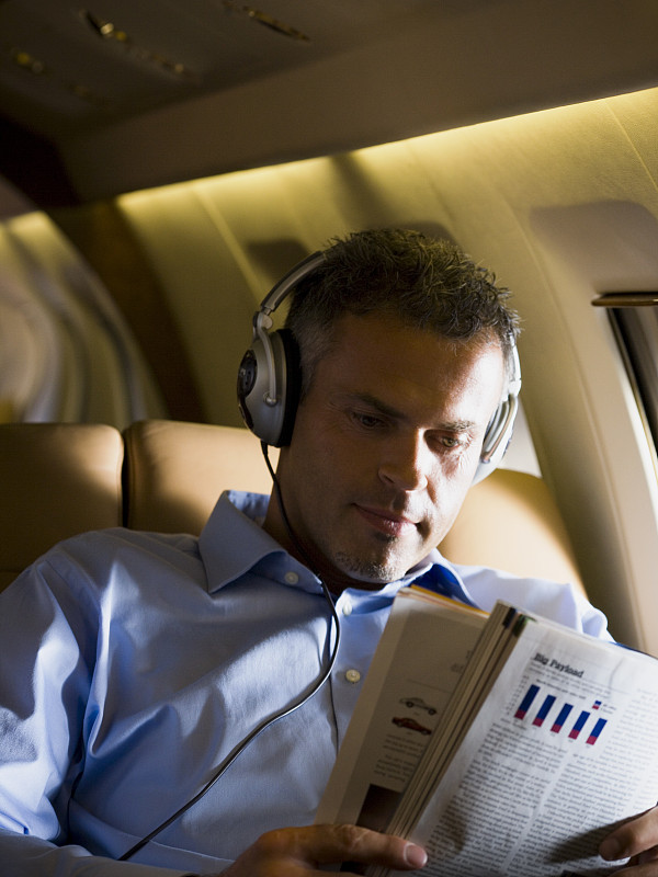 一个商人在飞机上戴着耳机听音乐，看杂志图片下载
