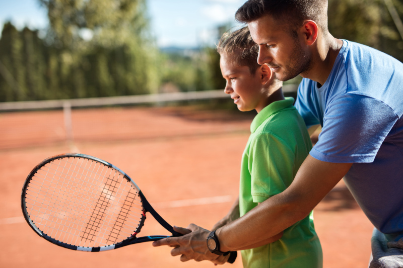 网球教练在网球场上帮助小男孩。图片下载