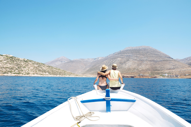 希腊，后视图的一对夫妇坐在船头手臂在看阿莫戈斯岛图片下载