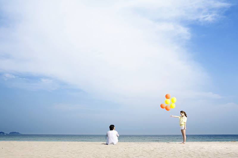 在海滩上，女人把气球递给男人。图片下载