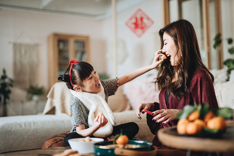 可爱的女儿在家里帮妈妈准备红包时，与妈妈分享传统小吃图片素材