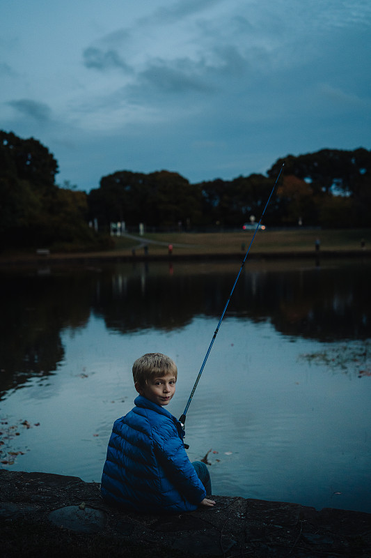 一个小男孩晚上钓鱼。图片下载