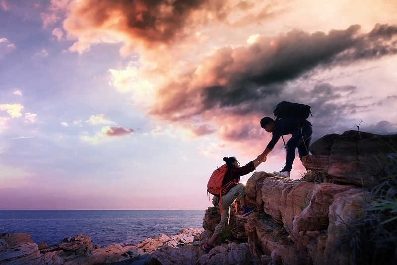 亚洲人伸出手帮助他的朋友上山。团队合作，帮助，攀登的概念。图片下载