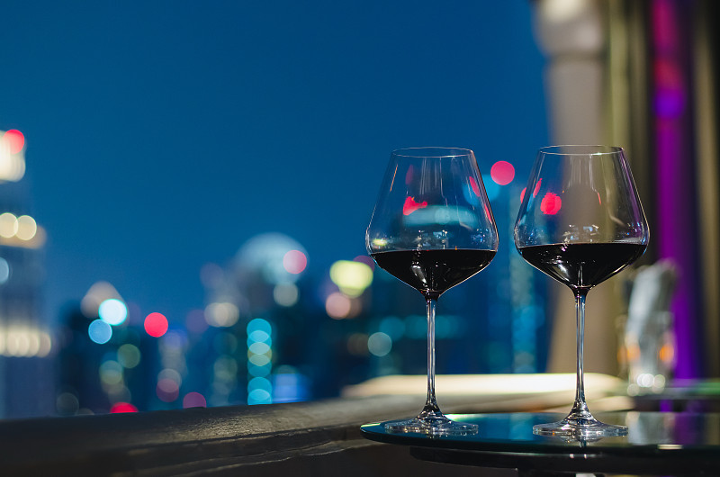 两杯红酒放在屋顶酒吧的桌子上。图片素材