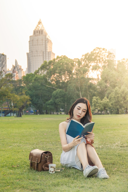 年轻女子在城市公园里放松地看书图片素材
