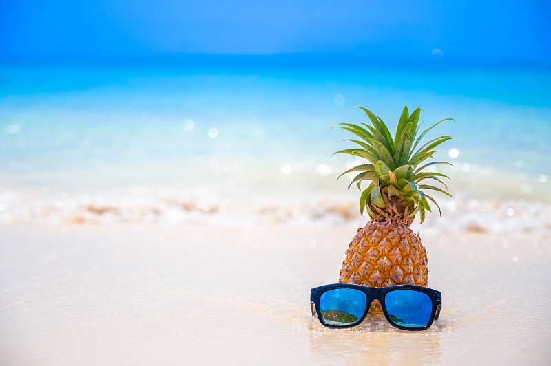 眼镜菠萝位于海边的海滩上，在炎热的阳光下，设置了夏季的概念。图片素材