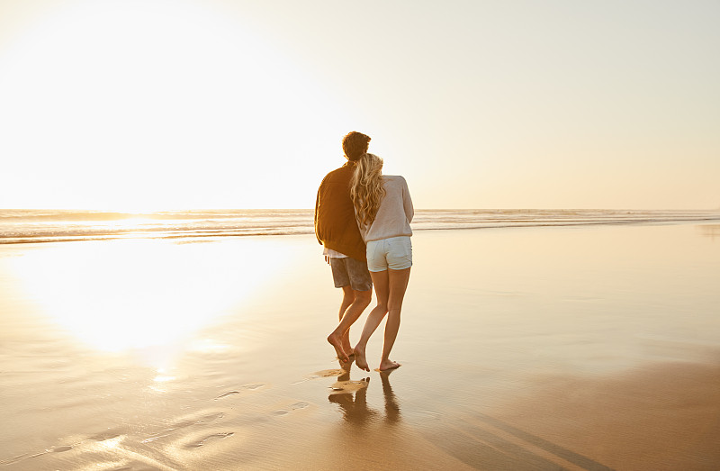 傍晚时分，一对年轻夫妇在海滩上散步图片素材