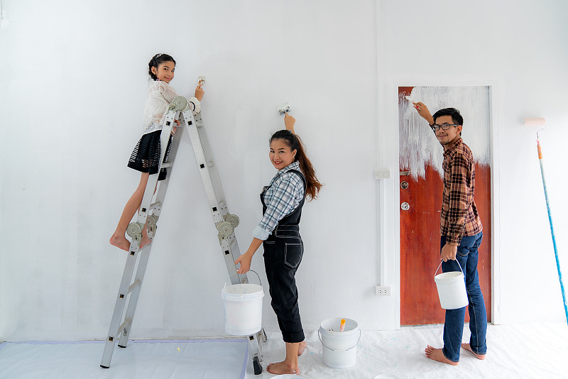幸福的亚洲家庭与父亲，母亲和女儿在粉刷粉刷白色的墙壁在他们的新房子。家庭生活爱情关系，还是新房活动概念图片素材