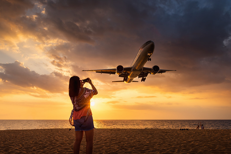 肖像迷人的女人在海滩上享受拍摄飞机降落在普吉岛国际机场。图片素材