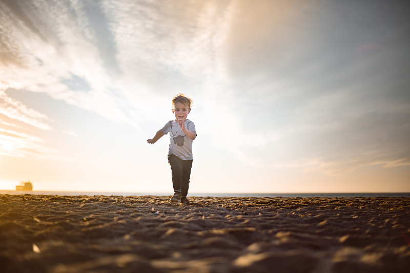 日落时分，男孩在海滩上朝着照相机跑去图片下载