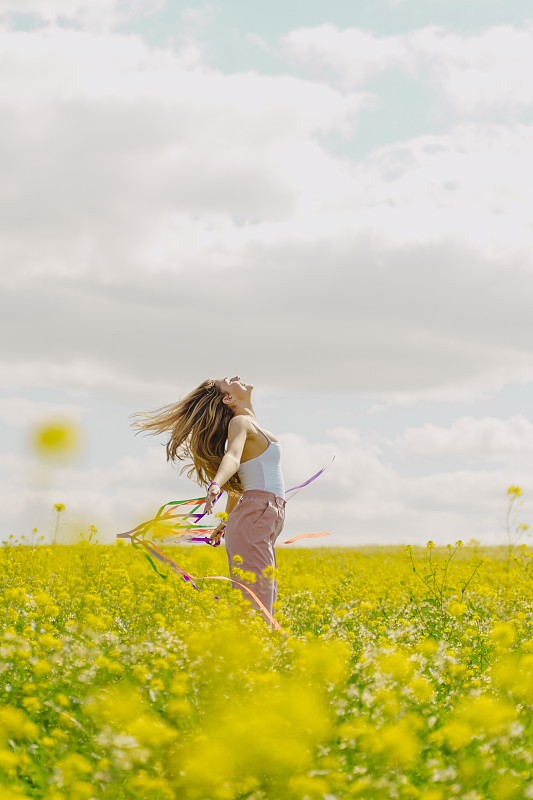 快乐的年轻女子在春天的鲜花草地上舞动着彩带图片下载