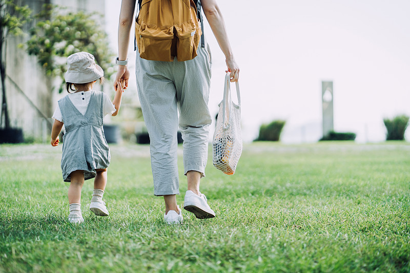裁剪的镜头，年轻的亚洲母亲携带杂货与棉网生态袋。在杂货店购物后和小女儿手牵手穿过公园。“零浪费”的概念图片下载