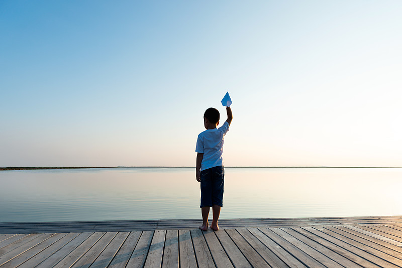 小男孩在湖边拿着纸飞机图片素材
