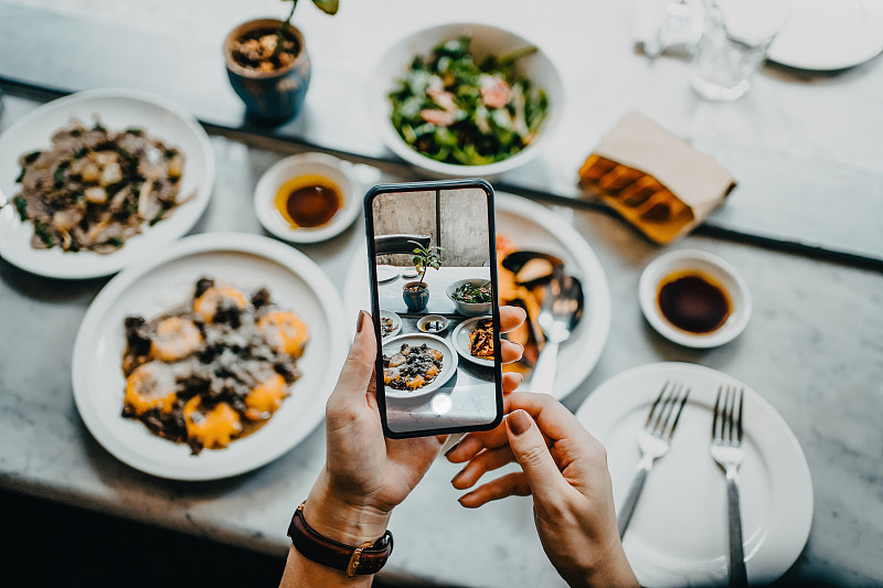 餐厅里，一位女士在用智能手机进食前用手拍下新鲜食物的俯视图图片下载