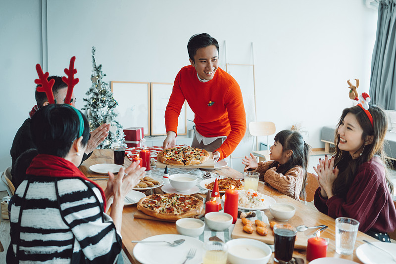 快乐的亚洲多代家庭一起庆祝圣诞节，微笑的年轻人在圣诞派对期间在家为家人提供食物图片下载