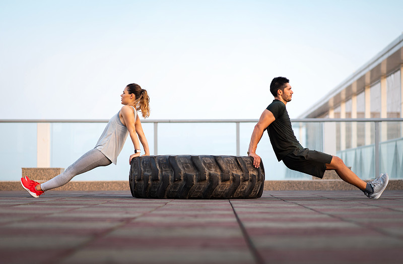 一对健身夫妇在户外锻炼时，在拖拉机轮胎上做三头肌俯卧撑图片下载