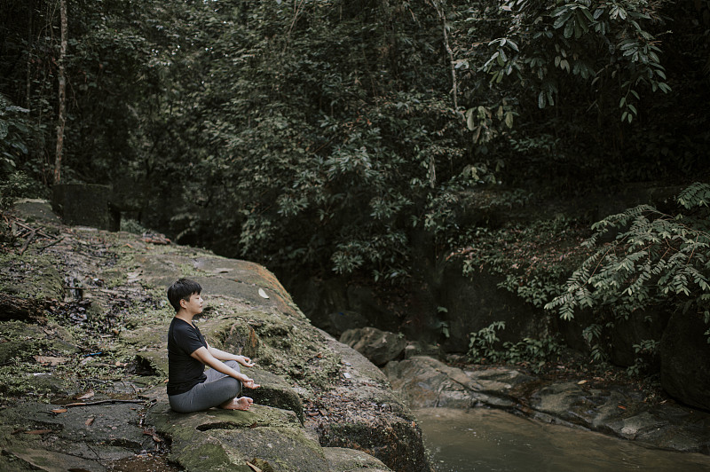 an asian chinese mid adult female meditating at the river bank in the forest图片素材