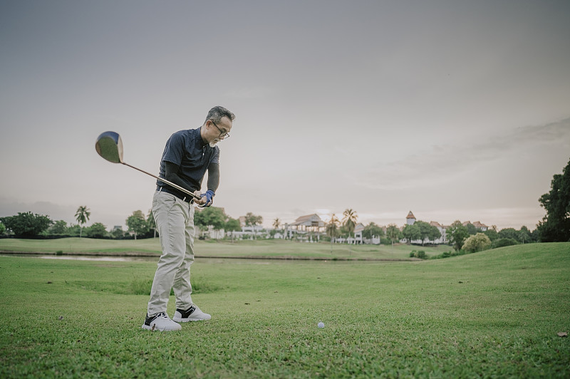 周末，一位成熟的亚洲华人男子在高尔夫球场开球，挥舞着他的球棒图片下载