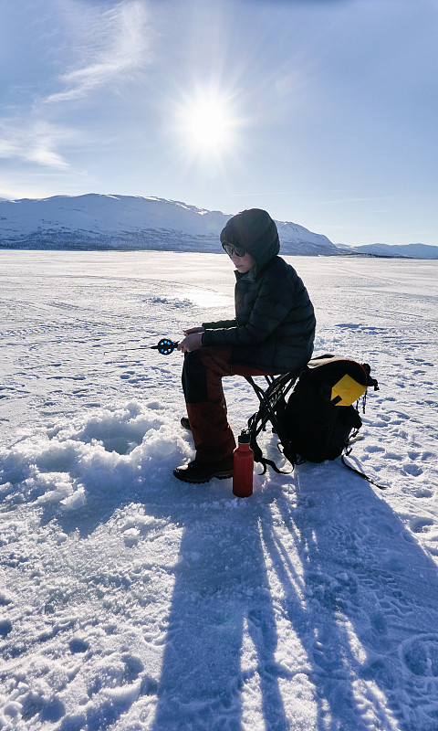Boy ice-fishing on frozen lake in Vasterbottens Lan, Sweden.图片素材