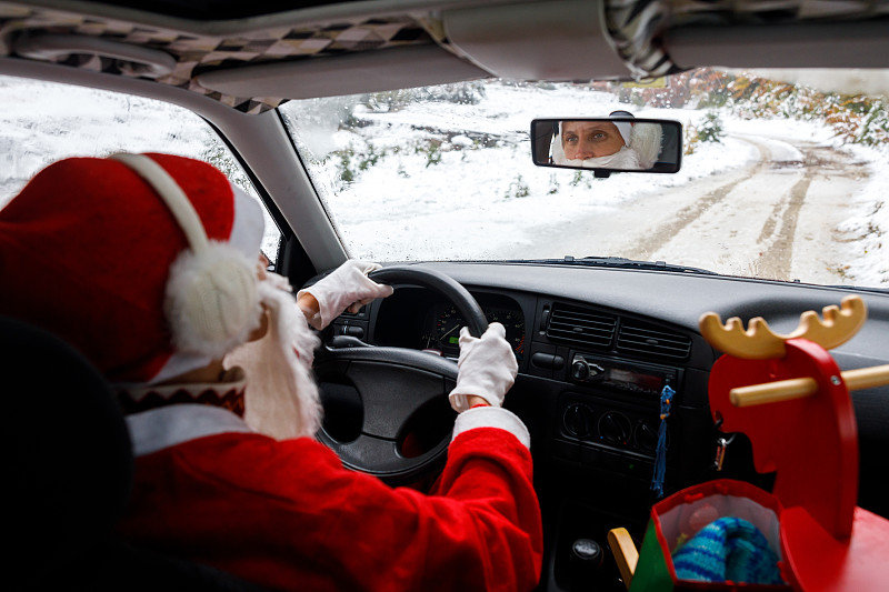 一名成年女子穿着圣诞老人服装，在白雪覆盖的乡村道路上驾驶汽车图片素材
