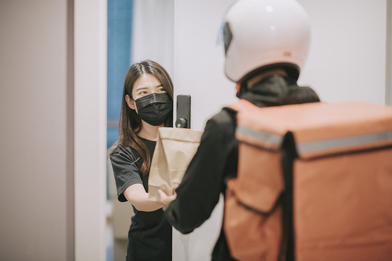 戴着头盔和外科口罩的亚裔华人送货员按门铃送食品图片下载